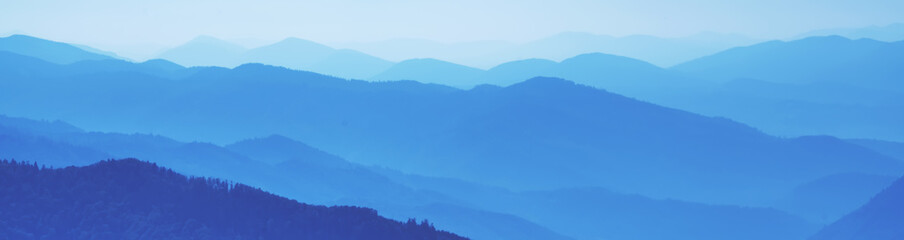 Fototapeta premium High peaks of beautiful blue mountain range landscape with fog and forest. Ukraine, Carpathians. Horizontal image.