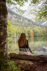Junge Frau sitzt alleine auf einem Baumstamm am See. Rückansicht, Aussicht genießen.