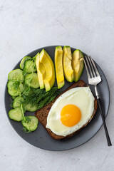 Delicious breakfast with avocado, fresh cucumbers and microgreens of peas with dill, fried eggs on black grain toast, top view