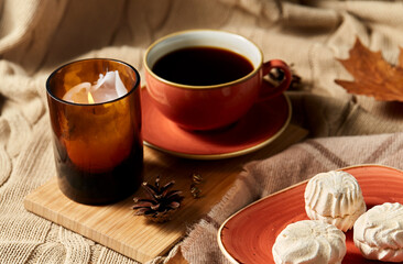 people, season and leisure concept - cup of coffee, autumn leaves, meringues and candle on warm blankets at home