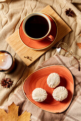 people, season and leisure concept - cup of coffee, autumn leaves, meringues and candle on warm blankets at home