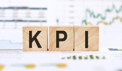 Word KPI - Key performance indicator, made with wood building blocks on background from financial graphs and charts.