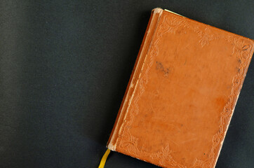 Very old worn notebook in brown leather binding. Vintage book on black background. Top view.