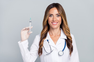 Photo of cheerful positive woman doc dressed white coat holding syringe smiling isolated grey color...