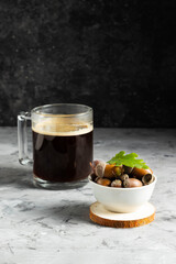 Alternative non-caffeinated drink in a glass mug with ripe acorns in a white plate on a dark background