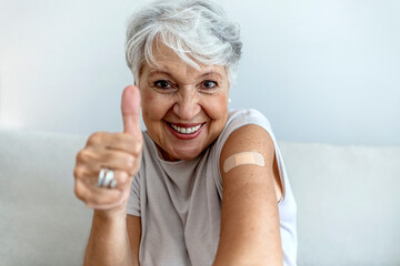 Cropped shot of a smile senior woman 70s after receiving the coronavirus covid-19 vaccine. Old aged woman posing with an adhesive COVID-19 and adhesive bandage on her upper arm. Vaccination concept. - obrazy, fototapety, plakaty