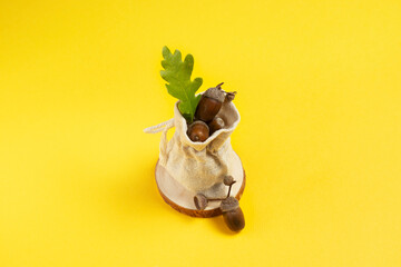 Ripe acorns in a linen bag with a green oak leaf on a yellow space copy background for text