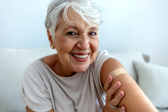 Proud mature woman smile after vaccination with bandage on arm. Beautiful smiling senior woman 70s after receiving the coronavirus vaccine. Elderly lady getting immunization via anti-viral vaccine.