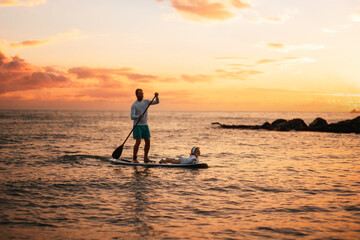 Family summer vacations. Silhouette of father and daughter surfing on a sup board. Sunset sky and...