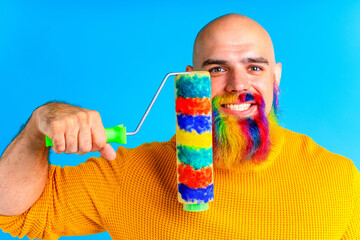 Portrait of handsome man with dyed beard on colors of rainbow holding roller tool for wall paint in...