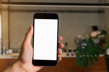 Hand holding white mobile phone with blank white screen in cafe.
