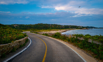 Curved two-lane coastal road and dramatic cloudscape along the Falmouth Height Beach on Cape Cod 