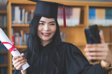 University graduate in graduation gown and mortarboard celebrates in a virtual graduation ceremony. Happy female student on her graduation day at home. Concept of online education