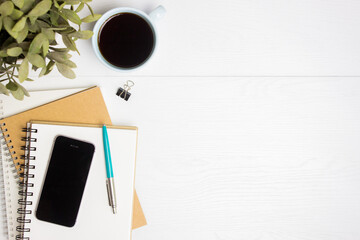 Working items on a table, coffee, phone, notebooks and pen on table.