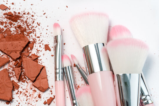 Creative photo of cosmetic swatches. Eye shadows in bronze colour broken and make up brushes on a white background 