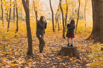 Fototapeta premium Mother photographer takes pictures of a her daughter in the park in autumn. Hobbies, photo art and leisure concept.