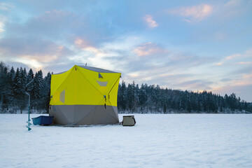 Ice fishing tent on a frozen lake at sunset. Fisherman camp on a peaceful winter evening.