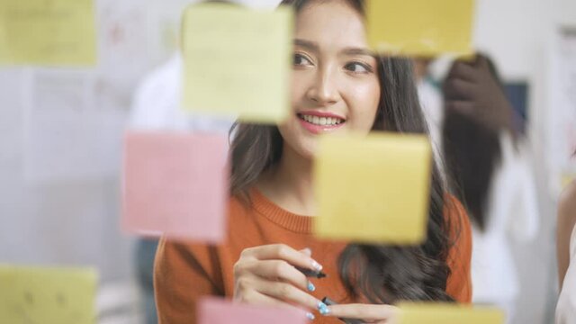 Asian business creative team meeting by use post it notes to share idea on glass wall.