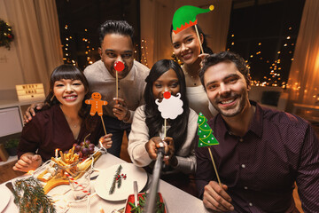 holidays, friendship and celebration concept - multiethnic group of happy friends having christmas dinner at home and taking selfie © Syda Productions