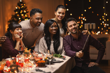 holidays, party and celebration concept - multiethnic group of happy friends having christmas dinner at home and taking selfie with smartphone