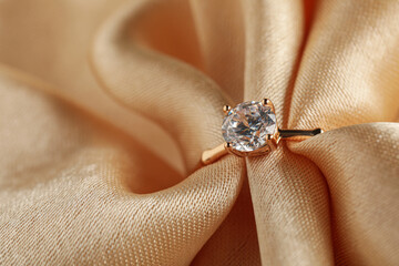 Beautiful engagement ring with gemstone on beige fabric, closeup