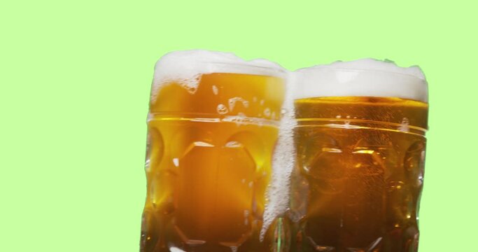 Celebration beer cheers concept - close up two swaying mugs or glasses of beer with foam isolated over abstract color background. Oktoberfest traditional party or victory competition or successful tas