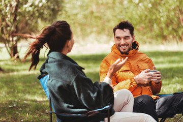 camping, tourism and travel concept - happy couple drinking tea at campsite