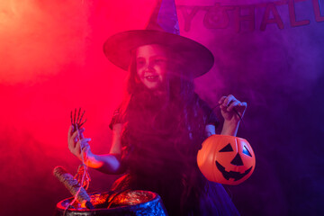 Child girl witch preparing a potion in the cauldron at halloween holidays.
