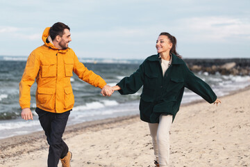 love, relationship and people concept - happy smiling couple running along autumn beach and holding hands