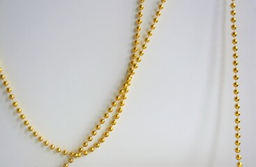 on a white background, a chain of gold beads hangs arbitrarily, the background