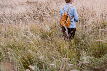 A young woman with a backpack on her back walks through the autumn field. Concept slow life.