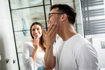 Young couple going through morning routine in the bathroom applying face cream.