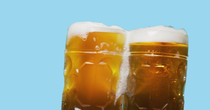 Celebration beer cheers concept - close up two swaying mugs or glasses of beer with foam isolated over abstract color background. Oktoberfest traditional party or victory competition or successful tas