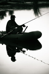 fisherman silhouette in a boat fishing on a lake at sunset