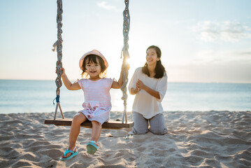 happy Little girl and mother swinging at the beach