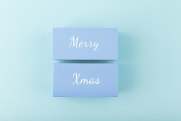 Merry Christmas minimal concept in light pastel blue colors. Handwritten text Merry Christmas on blue tablets against blue background. Modern trendy Merry Xmas concept