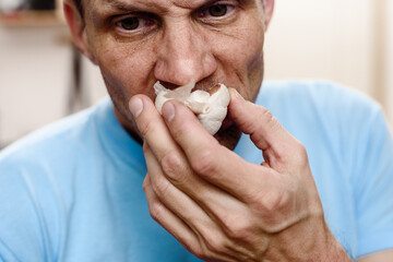 Young sick man smelling garlic while staying at home