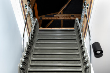 Folding metal stairs to the attic in the ceiling, open hatch and complex stairs, modern look.