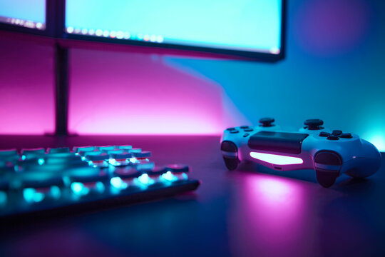 Low angle view of backlighted gaming accessories on dark table. Light blue and pink illuminated wall in background.