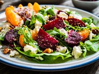 Beetroots salad with feta cheese, walnuts and tangerines on wooden background
