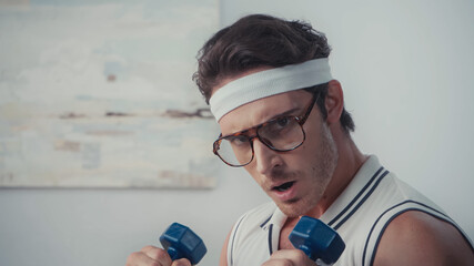 young sportsman in eyeglasses lifting dumbbells, retro sport concept