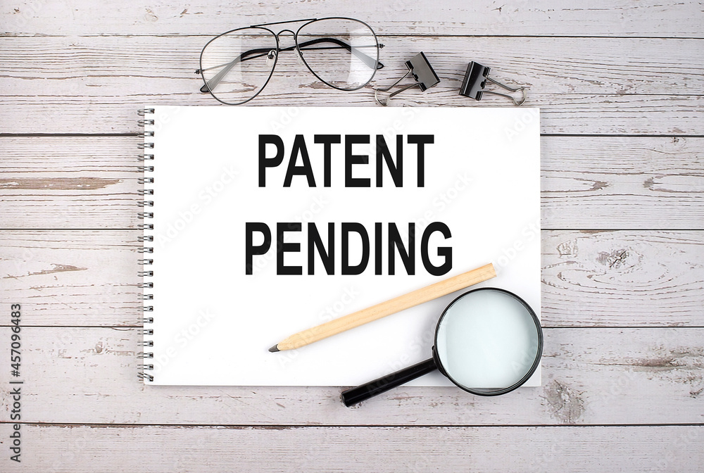 Aufkleber notebook with text patent pending on the wooden table with pen, magnifier and glasses