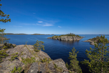 Landscape with a forest on stones over the lake. Sunny day at the lake. Reflection of the sky in the water. Pines on stones. The nature of the north.