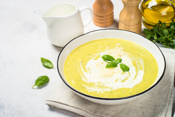 Zucchini soup with spinach and herb at white kitchen table.
