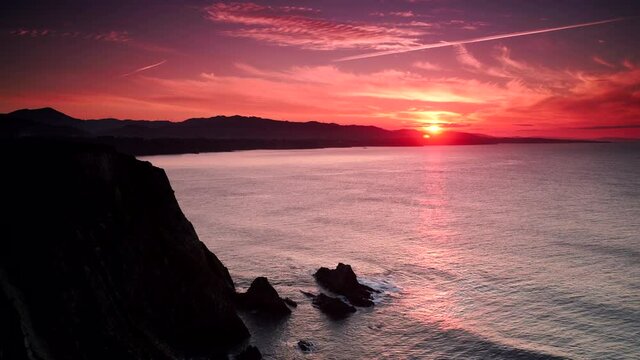 Timelapse. Sunset over rocky cliffs at Asturias coast in north Spain. View from Faro de Cabo Busto. Tourist attraction, place to visit.