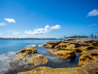 Fototapeta na wymiar Partly cloudy Spring afternoon on Sydney Harbour with nice rocks in the foreground the soft waves crashing on the shore and the beautiful harbour foreshore as a backdrop NSW Australia