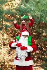 Santa Claus in glasses in a red fur coat against the background of a forest of a christmas tree a small child in an elf costume sits around the neck Santa's hands up screams joyfully for Christmas