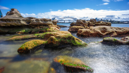 Fototapeta na wymiar Partly cloudy Spring afternoon on Sydney Harbour with nice rocks in the foreground the soft waves crashing on the shore and the beautiful harbour foreshore as a backdrop NSW Australia