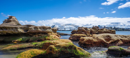Partly cloudy Spring afternoon on Sydney Harbour with nice rocks in the foreground the soft waves crashing on the shore and the beautiful harbour foreshore as a backdrop NSW Australia