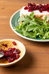 Aerial view of blue plate with cod pudding with mayonnaise, beetroot and arugula on wooden table, with bowl of beetroot, selective focus, vertical